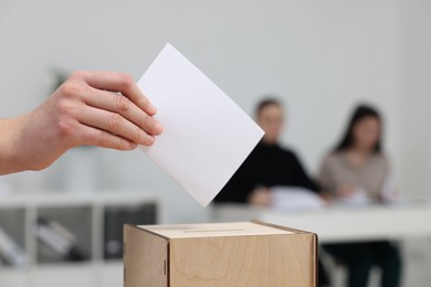 Photo of Woman putting her vote into ballot box on blurred background, closeup