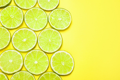 Photo of Juicy fresh lime slices on yellow background, flat lay. Space for text