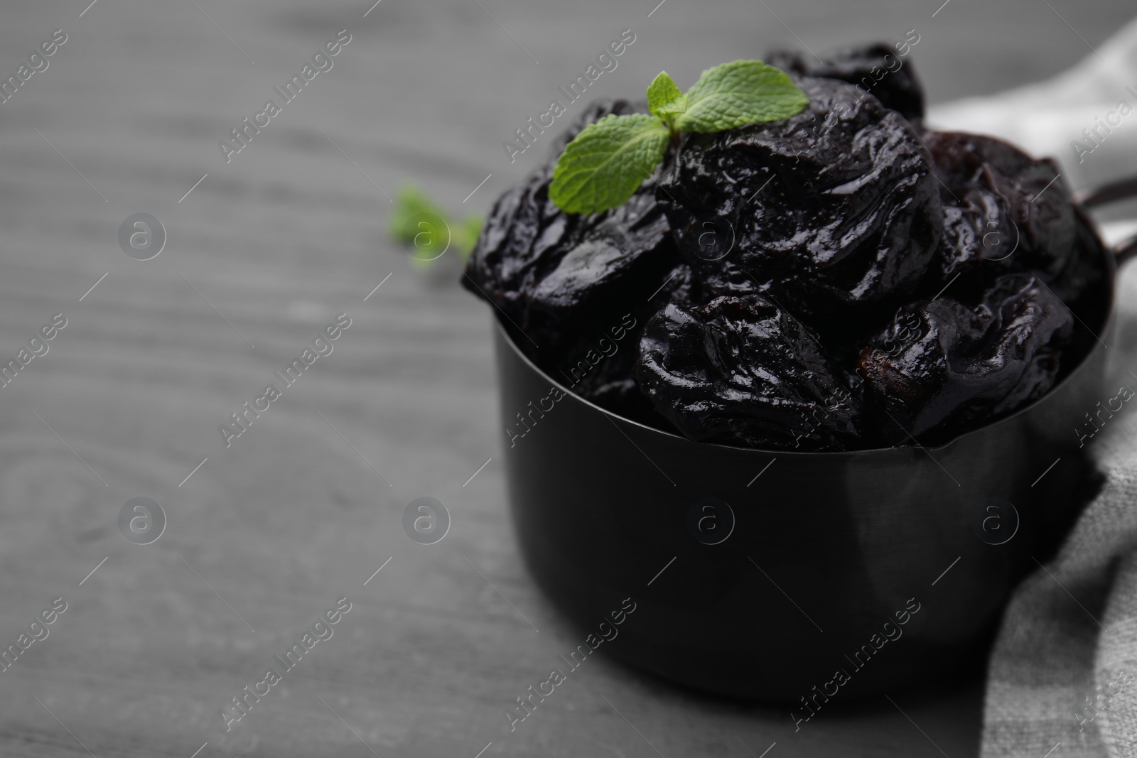 Photo of Sweet dried prunes and mint in scoop on grey wooden table, closeup. Space for text
