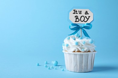 Photo of Beautifully decorated baby shower cupcake with cream and boy topper on light blue background. Space for text