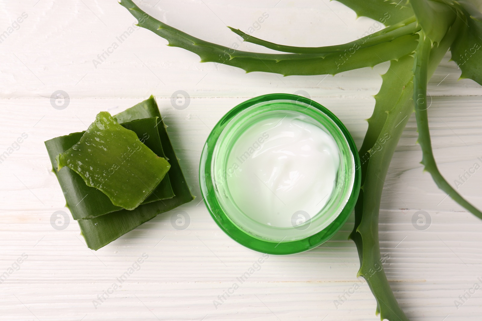 Photo of Jar of cosmetic cream and aloe vera leaves on white wooden table, flat lay