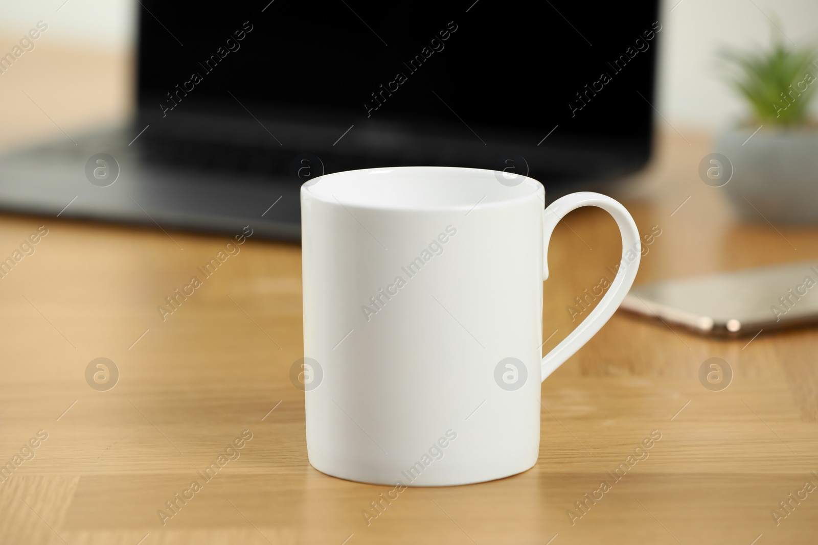 Photo of White ceramic mug on wooden table at workplace. Mockup for design