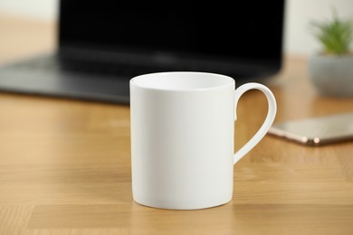 Photo of White ceramic mug on wooden table at workplace. Mockup for design