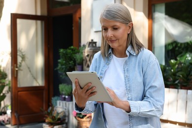 Photo of Beautiful business owner using tablet near her flower shop outdoors, space for text