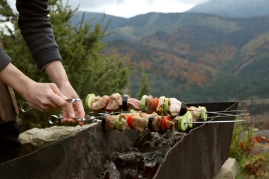 Photo of Woman cooking meat and vegetables on brazier against mountain landscape, closeup