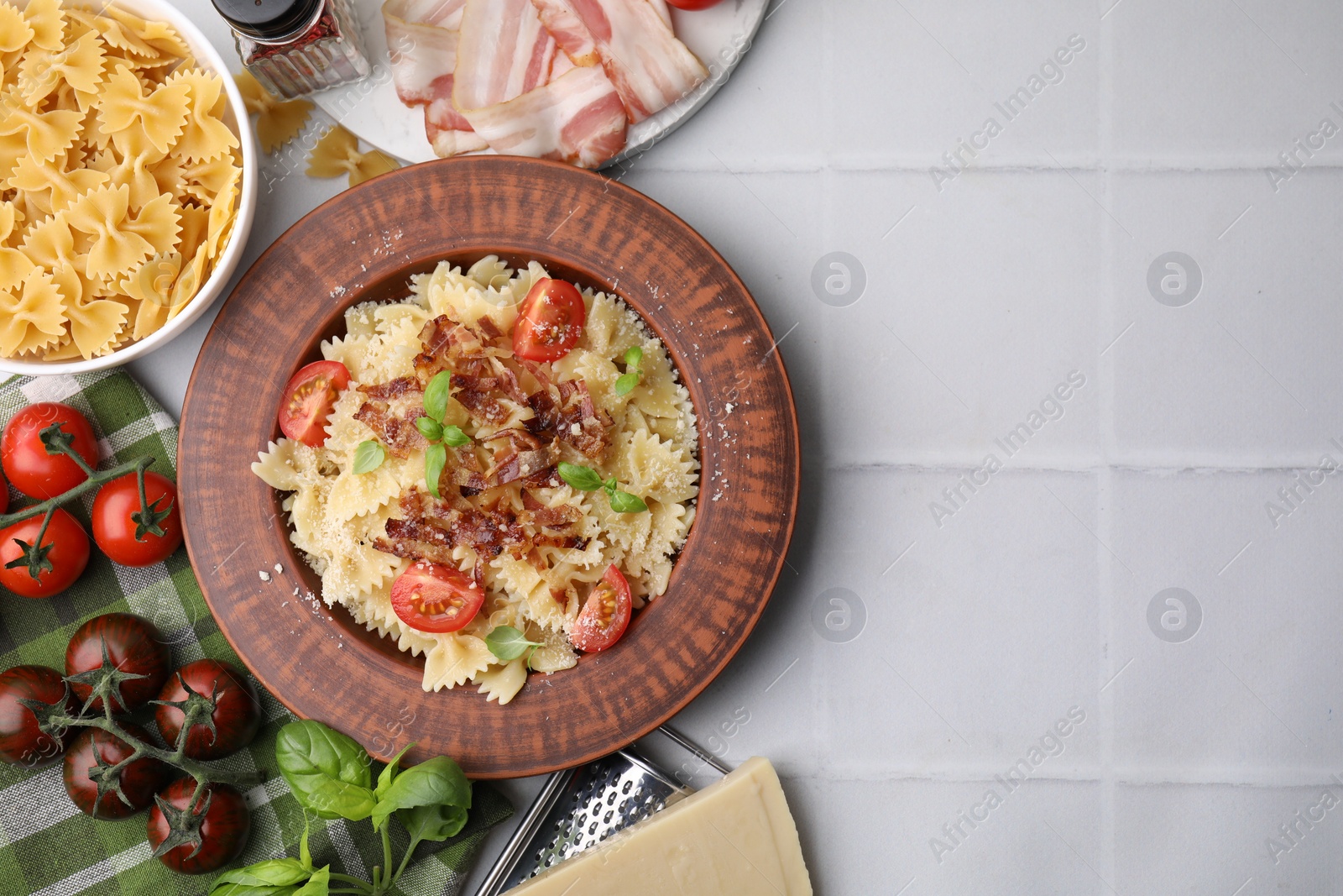 Photo of Tasty pasta with bacon, tomatoes and basil on white tiled table, flat lay. Space for text