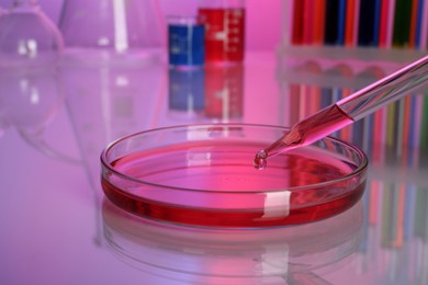 Dripping red reagent into Petri dish with sample on table, closeup