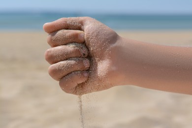 Photo of Child pouring sand from hand on beach, closeup. Fleeting time concept