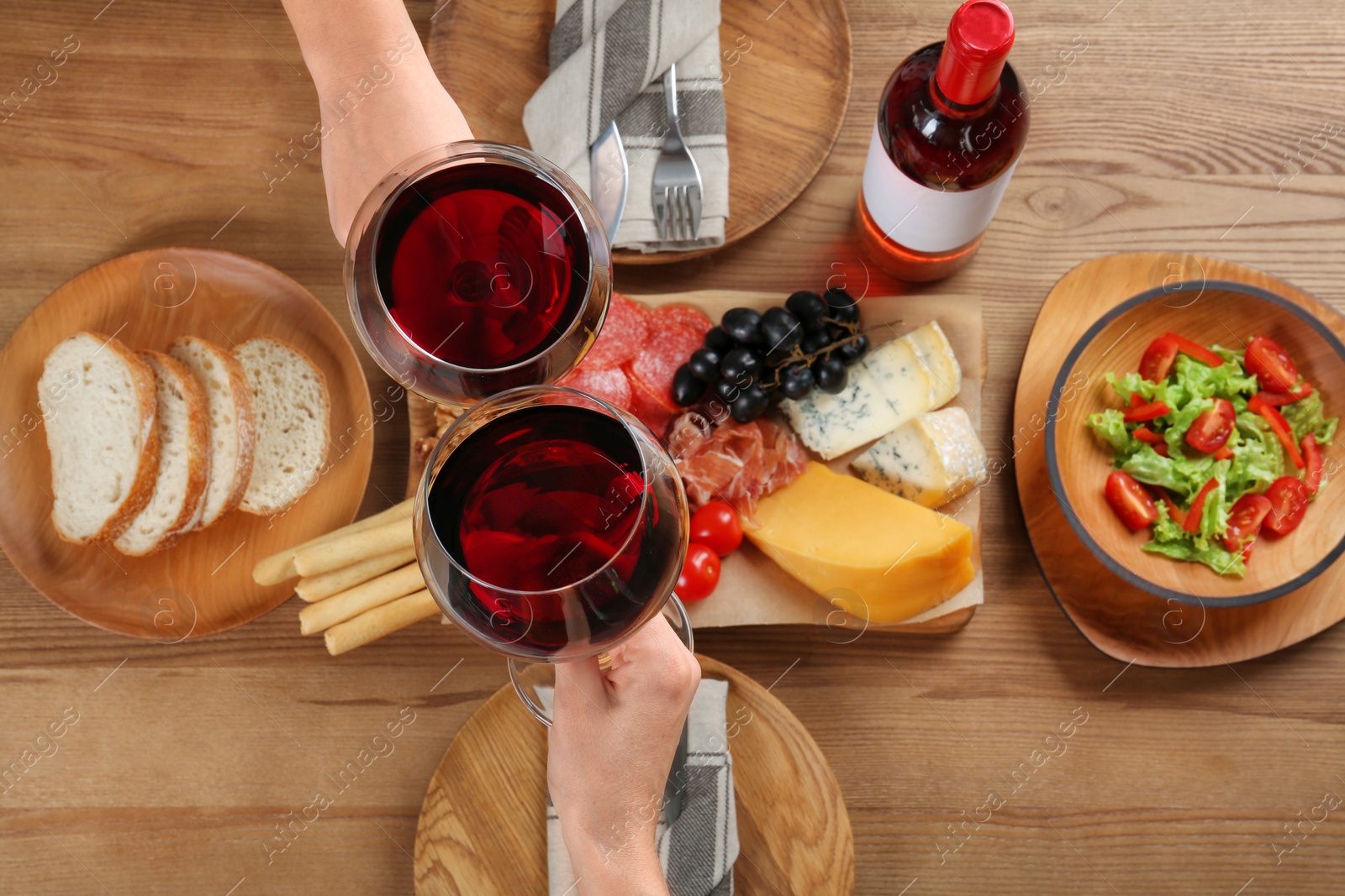 Photo of People holding glasses of red wine over table with delicious food, top view