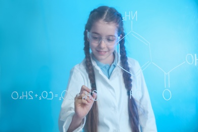 Schoolgirl writing chemistry formula on glass board against color background