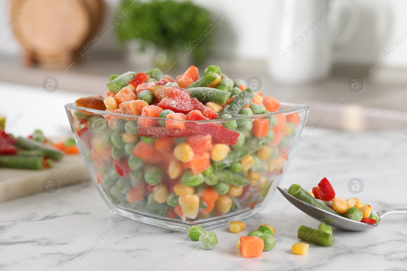 Photo of Mix of different frozen vegetables in glass bowl on white marble countertop, closeup
