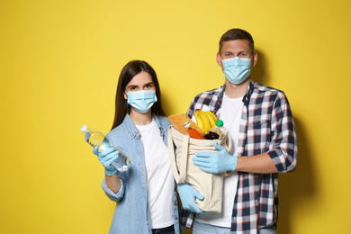 Photo of Volunteers in protective masks and gloves with products on yellow background. Aid during coronavirus quarantine