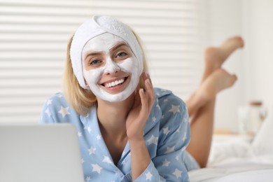 Young woman with face mask using laptop at home. Spa treatments