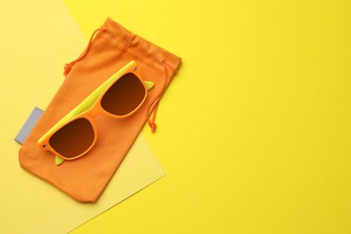 Stylish sunglasses with bag on yellow background, top view. Space for text