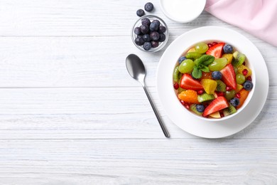 Photo of Delicious fresh fruit salad in bowl on white wooden table, flat lay. Space for text