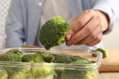 Man putting fresh broccoli into glass container at table, closeup. Food storage