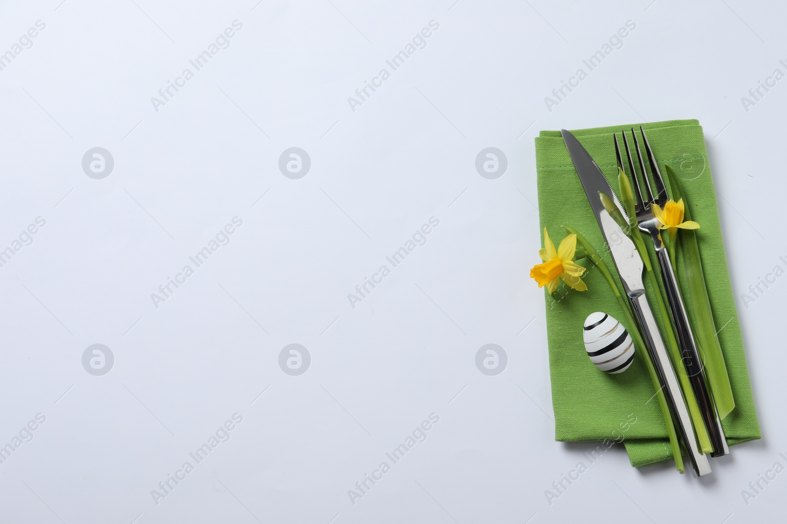 Photo of Cutlery set, Easter egg and narcissuses on white background, top view with space for text. Festive table setting