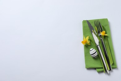 Cutlery set, Easter egg and narcissuses on white background, top view with space for text. Festive table setting