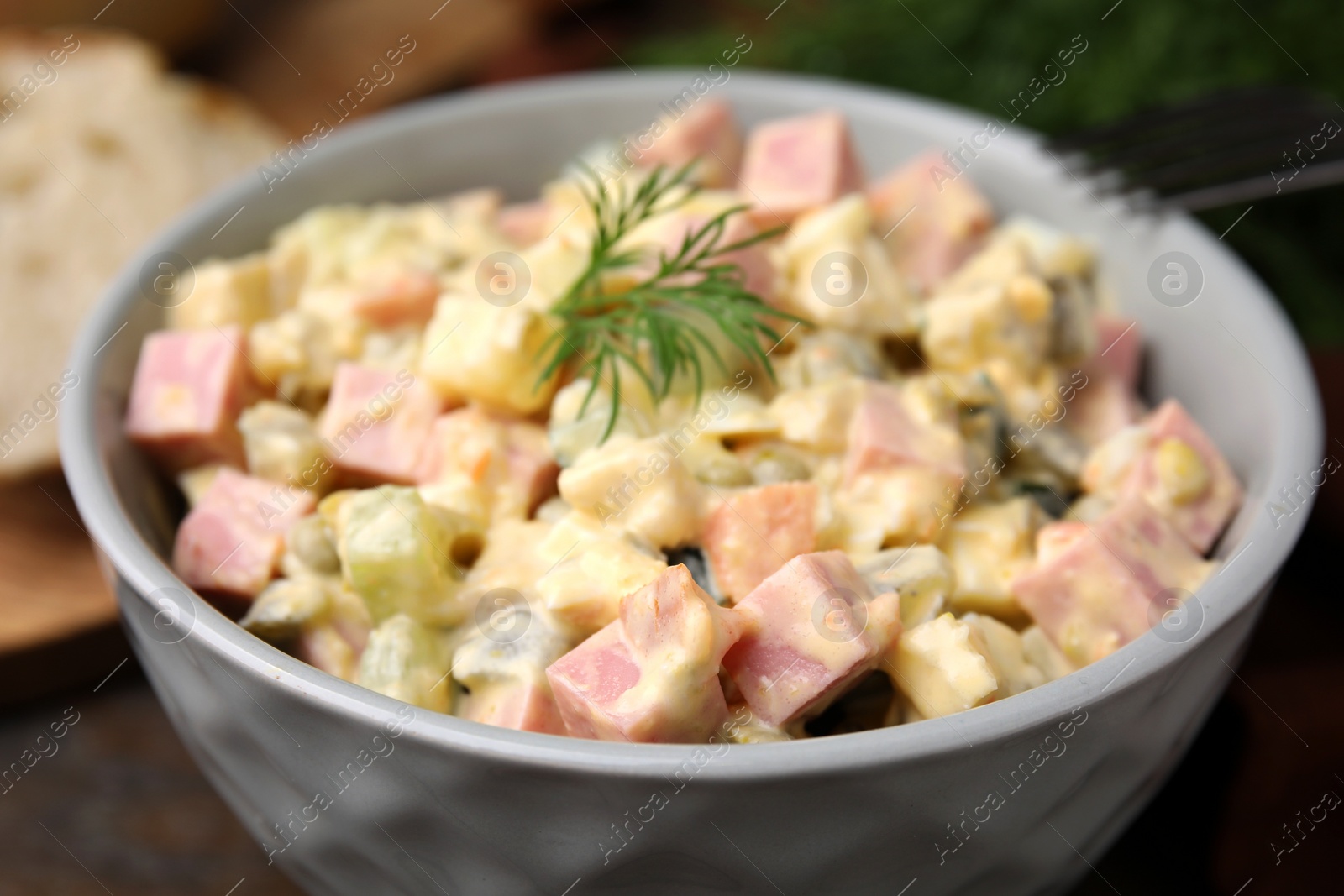 Photo of Tasty Olivier salad with boiled sausage in bowl on table, closeup