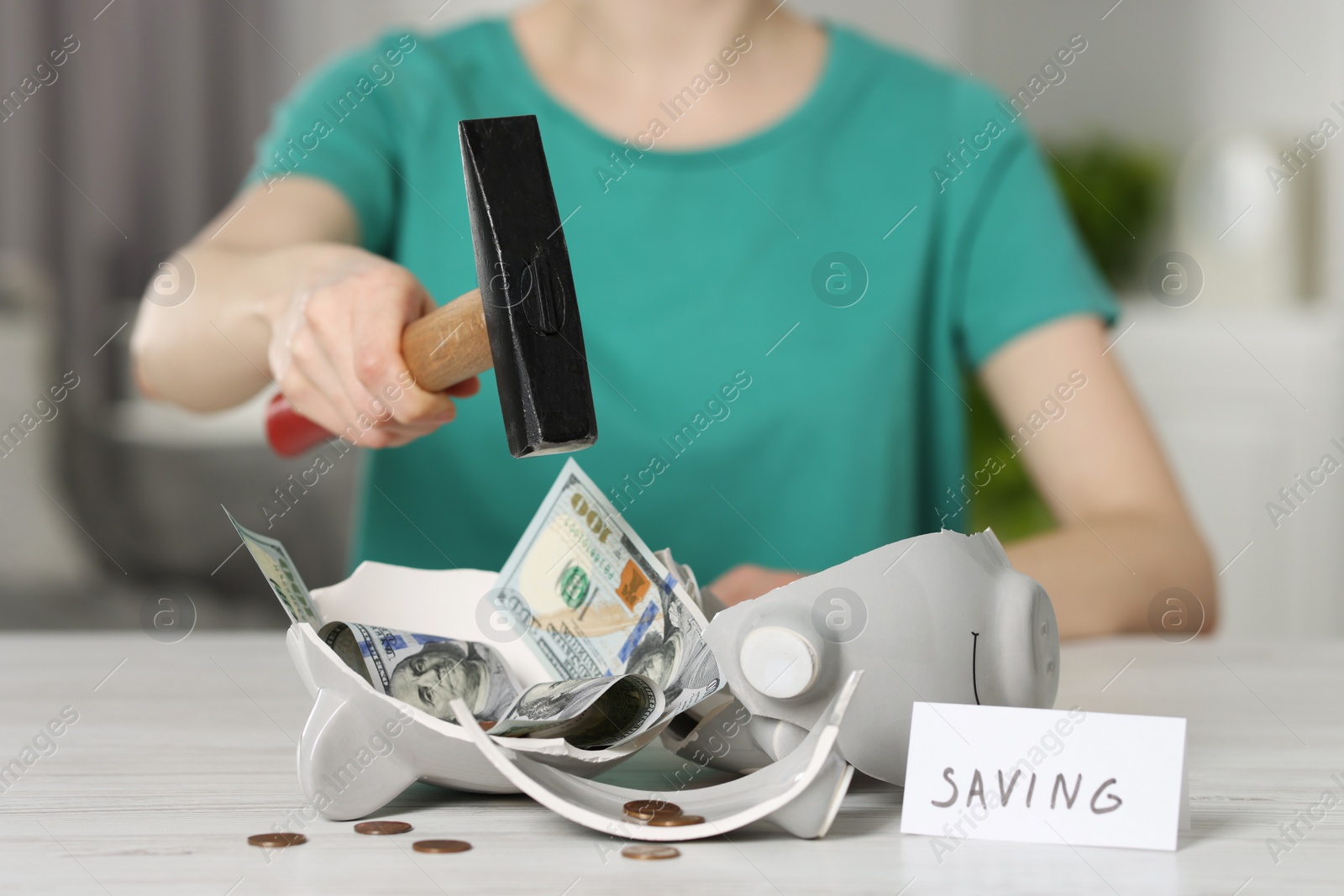 Photo of Financial savings. Woman breaking piggy bank with hammer at table indoors, closeup