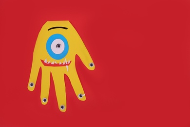 Photo of Funny yellow hand shaped monster on red background, top view with space for text. Halloween decoration