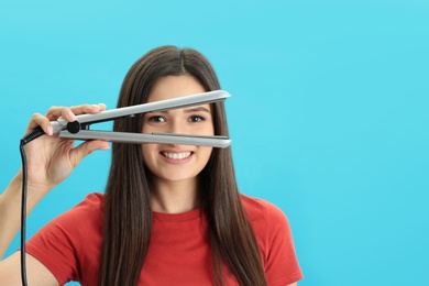 Young woman with modern hair iron on blue background, space for text