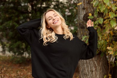 Happy woman in stylish warm sweater near tree outdoors