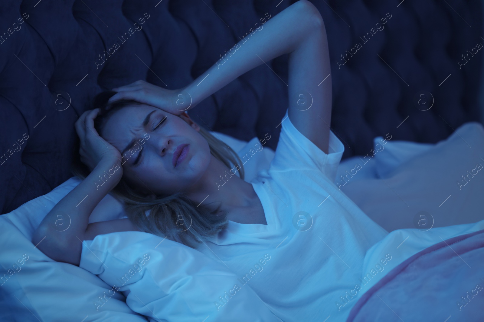 Photo of Young woman suffering from headache while lying in bed at night. Sleeping problems