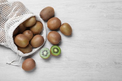 Net bag with cut and whole fresh kiwis on white wooden table, flat lay. Space for text