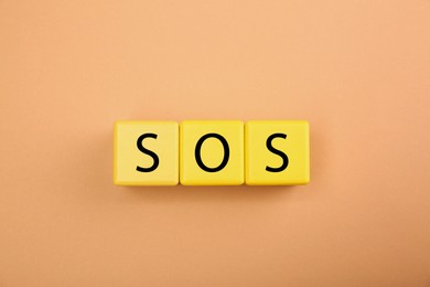 Photo of Abbreviation SOS (Save Our Souls) made of yellow cubes with letters on pale coral background, top view