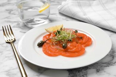 Photo of Salmon carpaccio with capers, microgreens and lemon served on white marble table