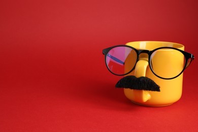 Man's face made of cup, fake mustache and glasses on red background. Space for text
