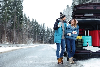 Photo of Couple near open car trunk full of luggage on snowy road, space for text