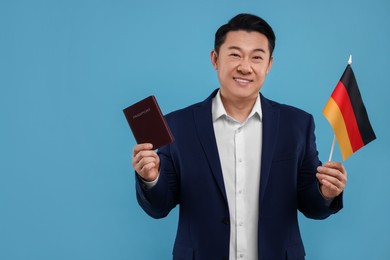 Photo of Immigration. Happy man with passport and flag of Germany on light blue background, space for text