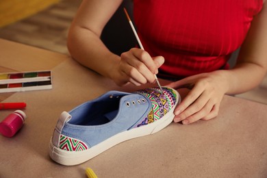 Woman painting on sneaker at wooden table indoors, closeup. Customized shoes
