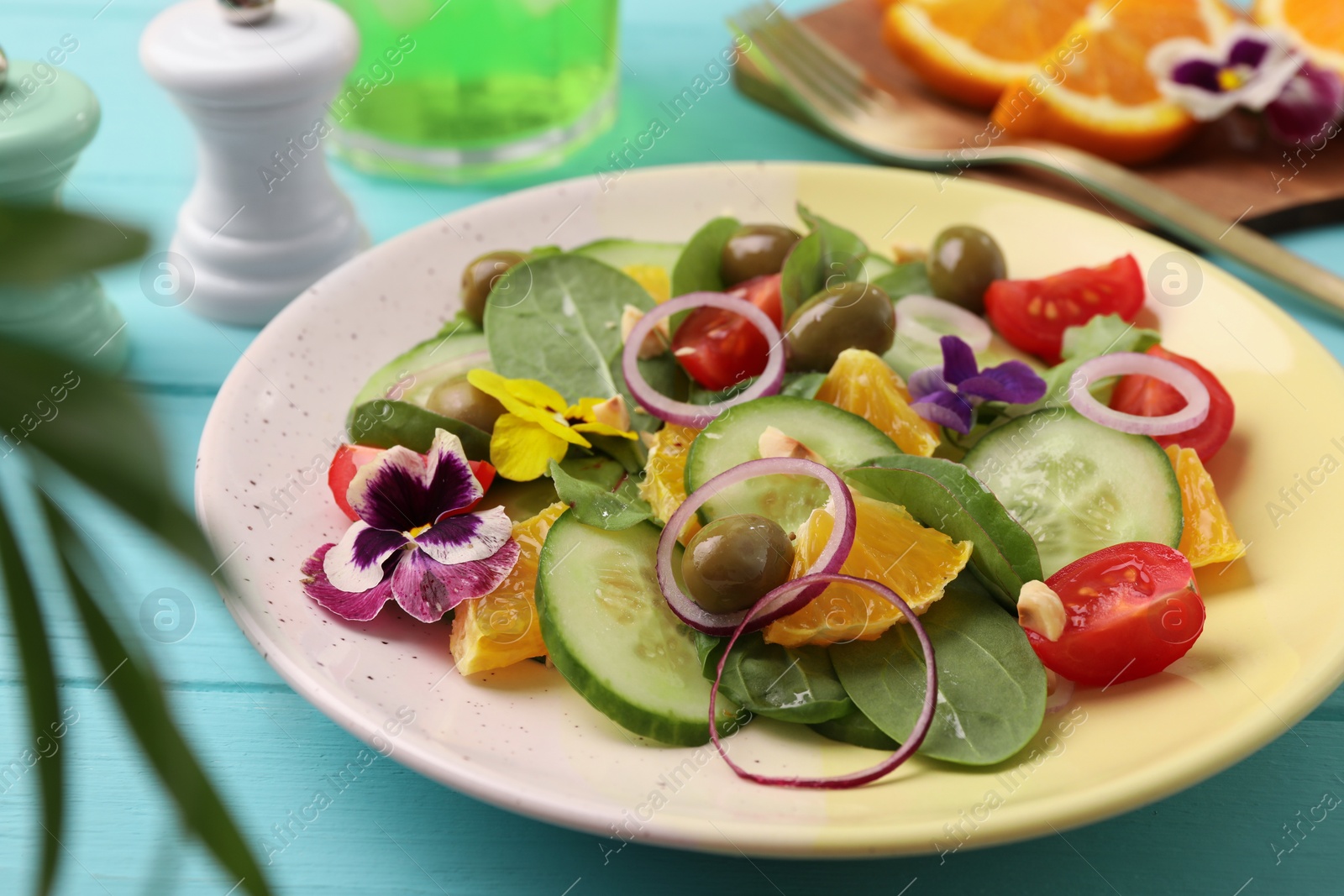 Photo of Delicious salad with orange, spinach, olives and vegetables served on turquoise wooden table, closeup