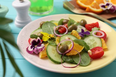 Delicious salad with orange, spinach, olives and vegetables served on turquoise wooden table, closeup