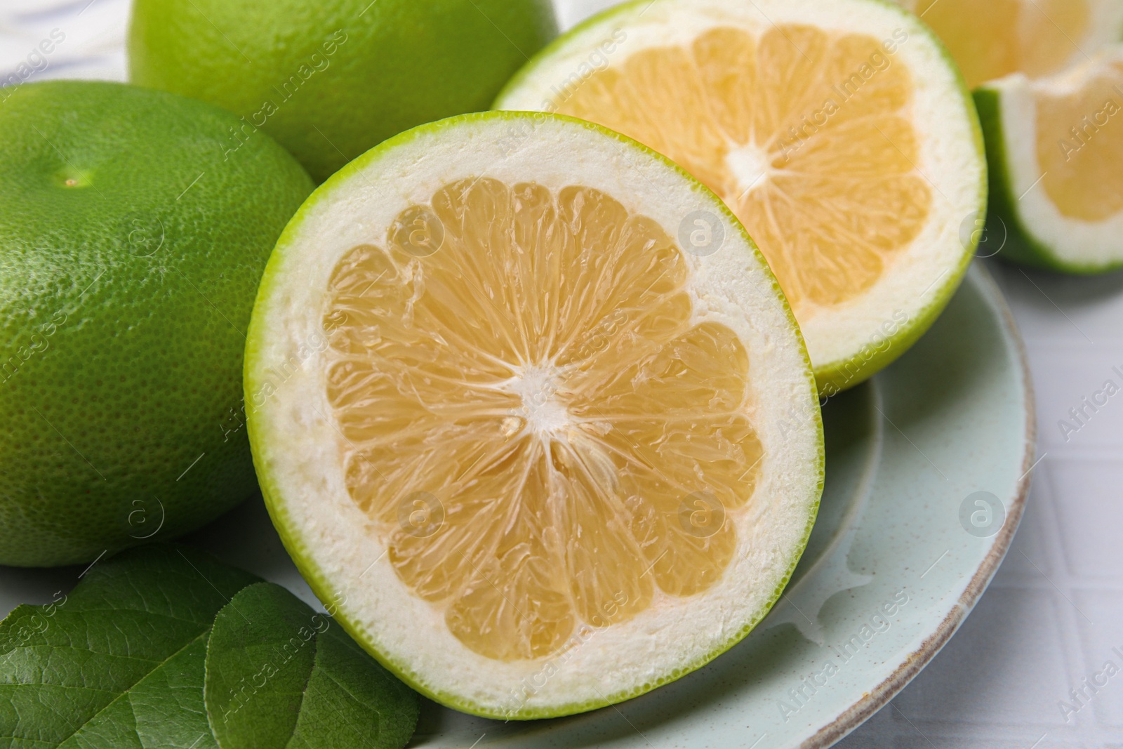 Photo of Whole and cut sweetie fruits with green leaves on white tiled table, closeup