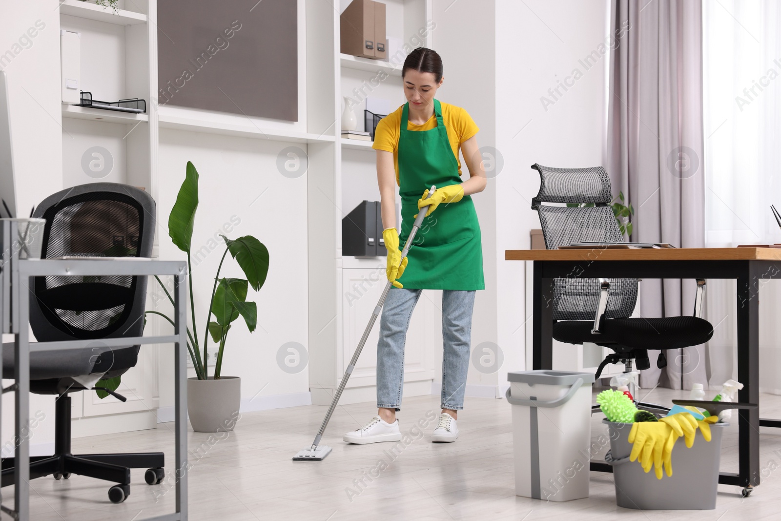 Photo of Cleaning service worker washing floor with mop. Bucket with supplies in office