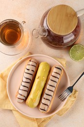 Different tasty glazed eclairs and tea served on color textured table, flat lay