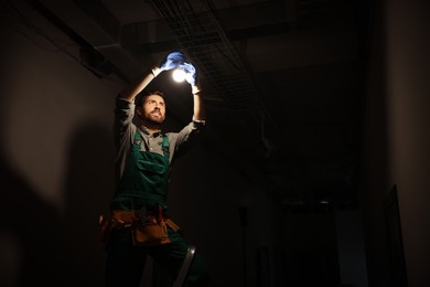 Photo of Electrician changing light bulb indoors in darkness