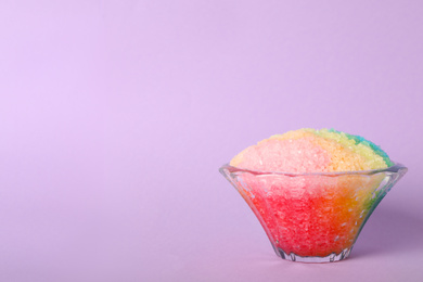 Rainbow shaving ice in glass dessert bowl on violet background, space for text