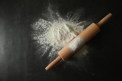 Photo of Scattered flour and rolling pin on black table, top view