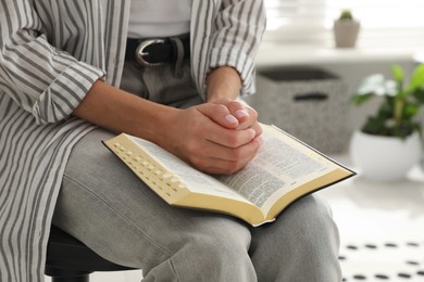 Photo of Young woman praying over Bible at home, closeup