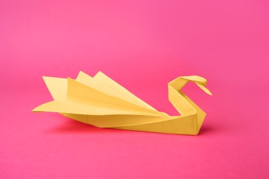 Photo of Yellow paper swan on pink background. Origami art