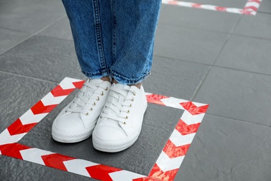 Photo of Woman standing on taped floor marking for social distance, closeup. Coronavirus pandemic