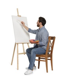Photo of Man with brush painting against white background. Using easel to hold canvas