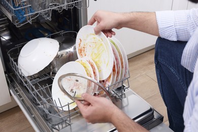 Man loading dishwasher with dirty plates indoors, closeup