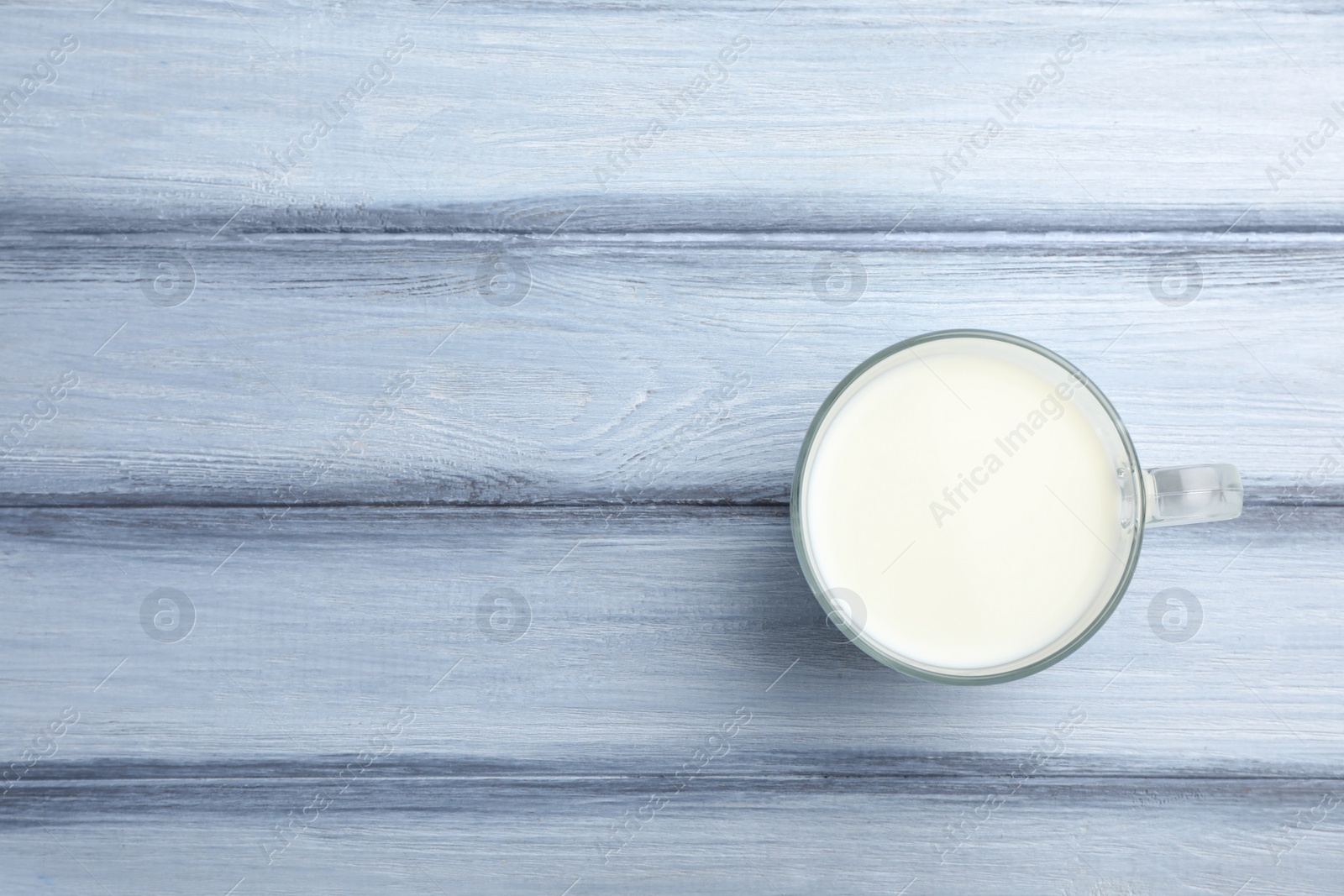 Photo of Cup of fresh milk on wooden table, top view. Space for text