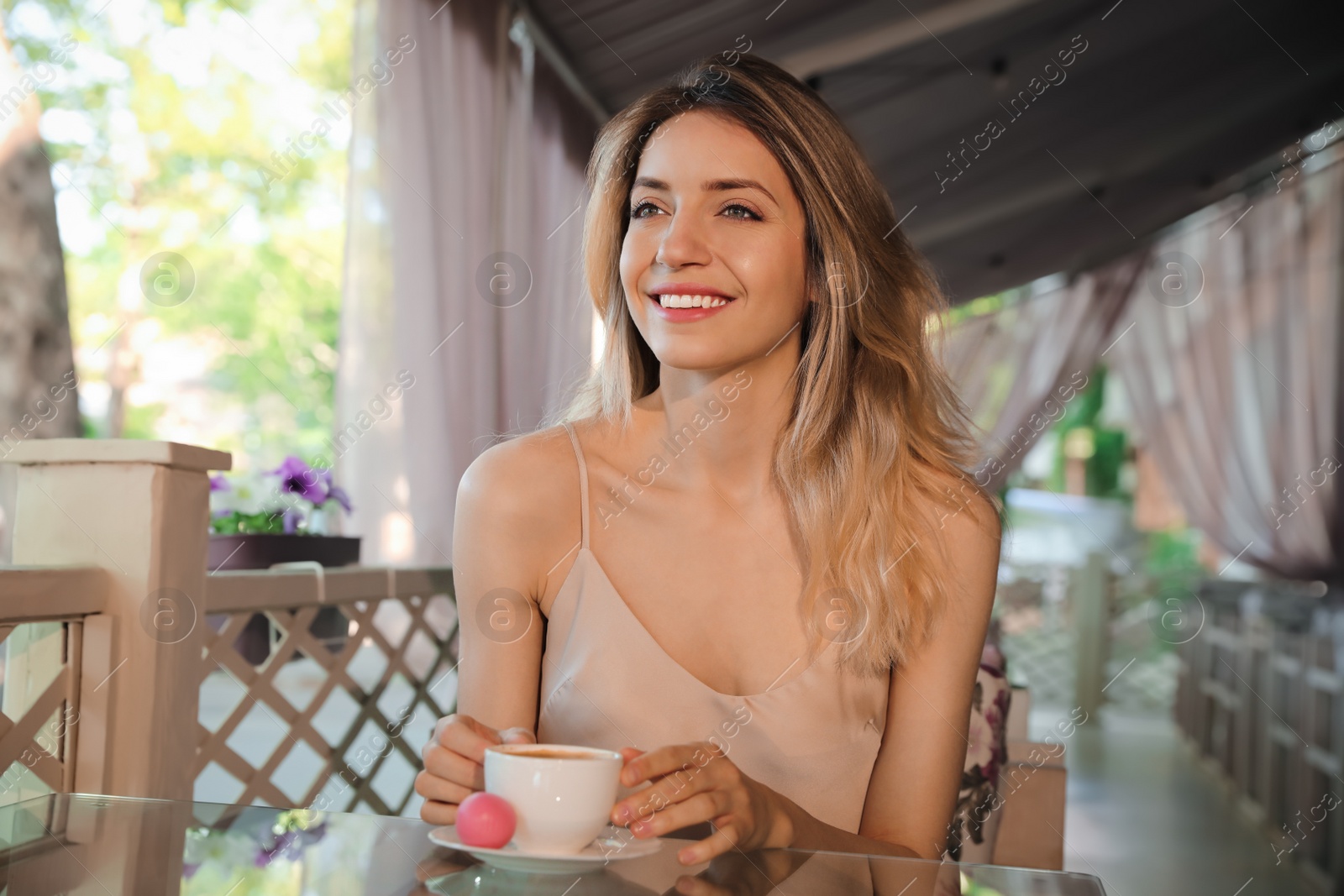 Photo of Happy young woman with cup of coffee enjoying early morning on cafe terrace